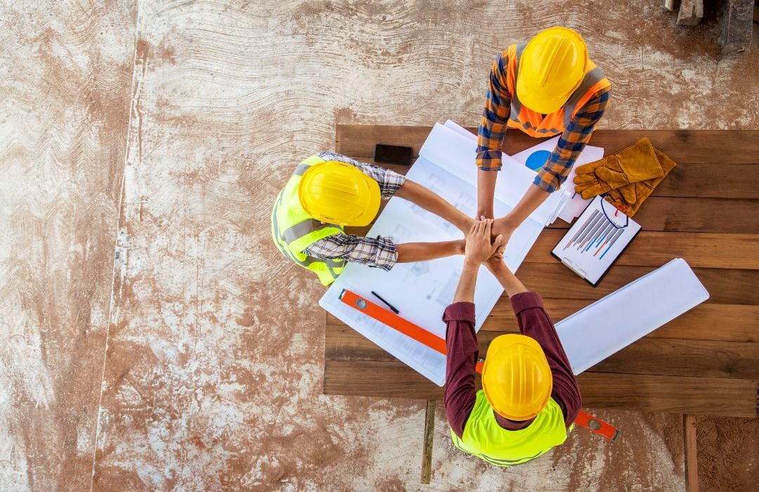 Birds eye view of a three person construction crew huddling over a blueprint Birds eye view of a three person construction crew huddling over a blueprint
