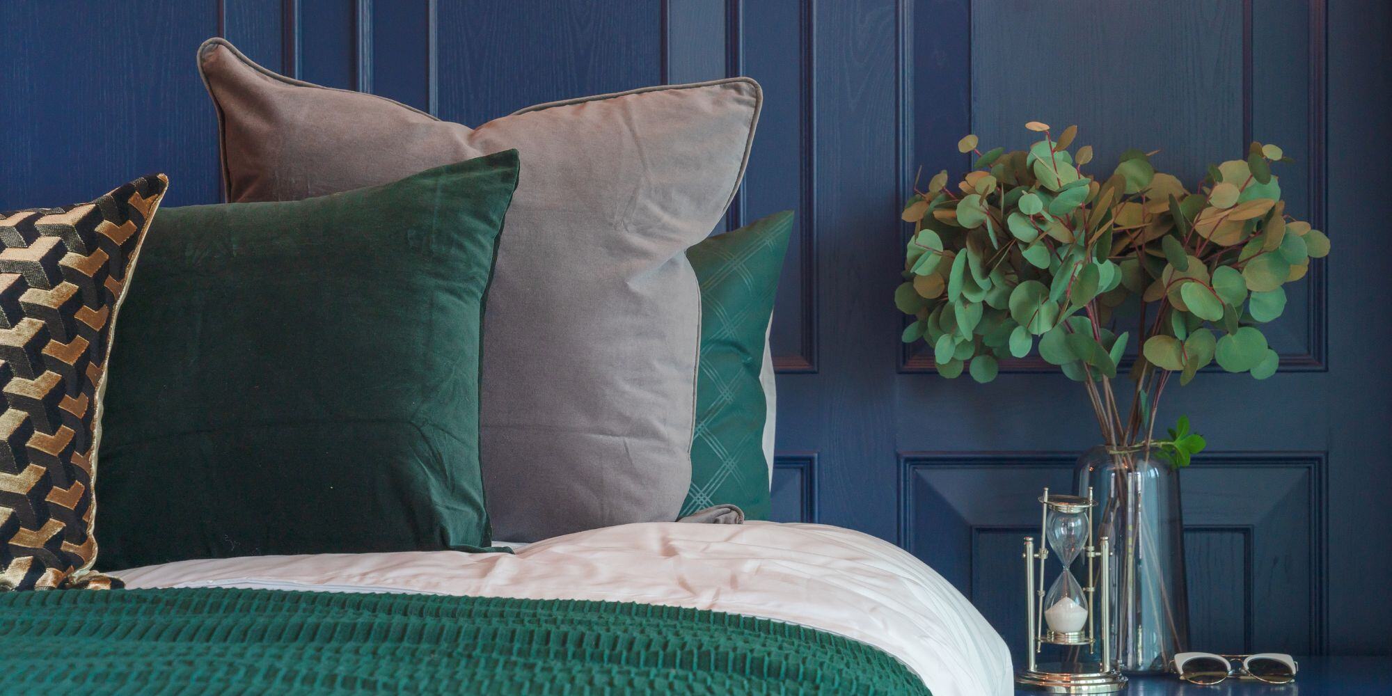 master bedroom with with green and gray pillows, plan on a side table, and dark blue box trimmed walls