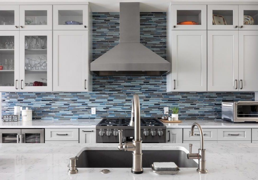 Remodeled kitchen with white cabinets, multi color blue backsplash and stainless steel appliances